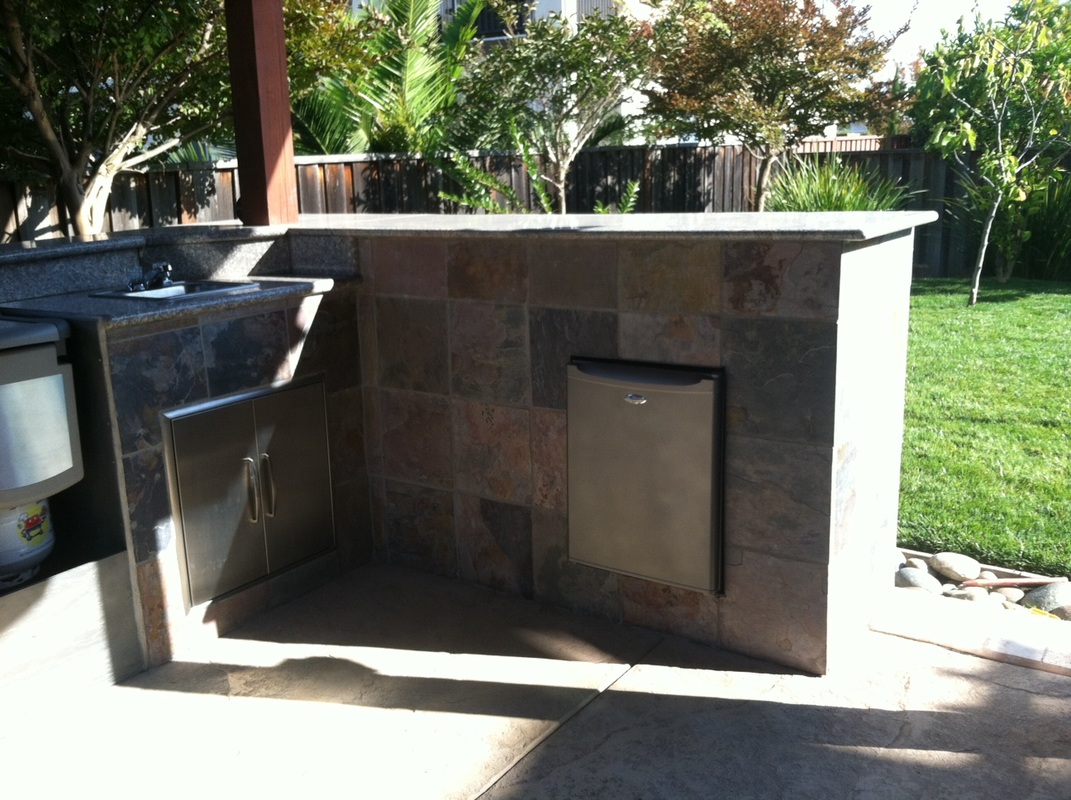 Built-in outdoor kitchen with slate tile, stainless cabinets, and refrigerator